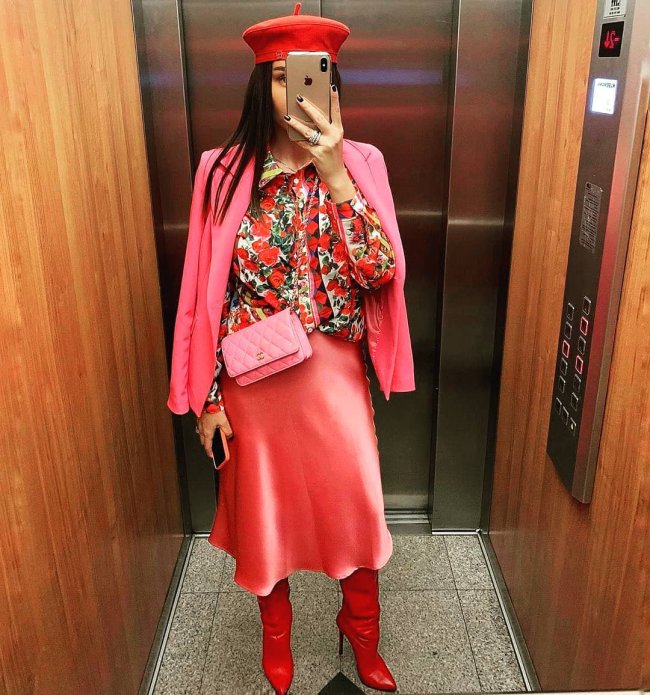 outfit rosa e vermelho Jovem tirando foto em elevador, mostrando seu visual com boina, camisa estampada, blazer rosa e saia.