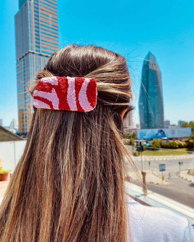 presilha rosa e vermelho Na imagem só podemos ver alguém de costa, com o cabelo preso com uma presilha rosa com detalhes em vermelho.