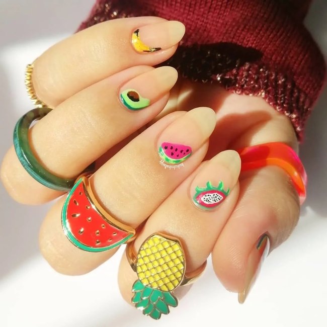 Foto com close nas unhas e tem nail art com desenhos de frutas como melancia, abacaxi, kiwi, abacate e banana.