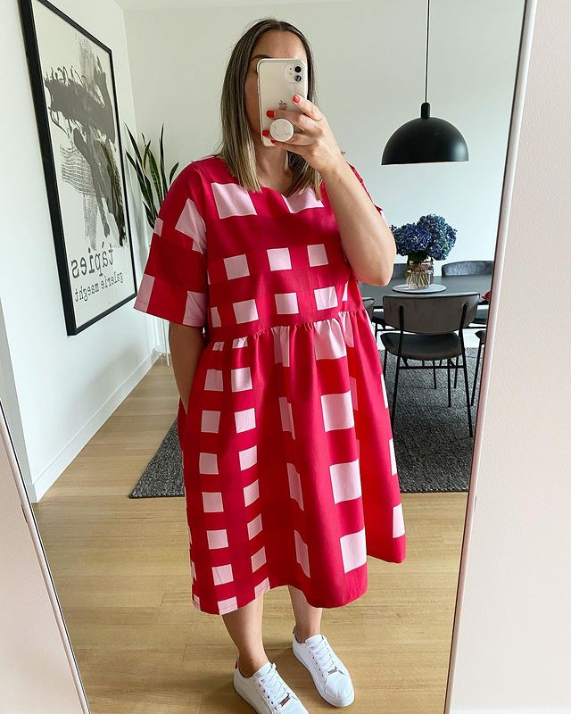 Jovem posando para foto no espelho usando vestido quadriculado vermelho e rosa.