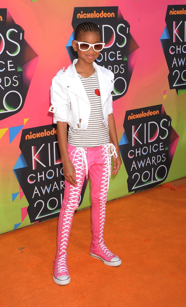 Nickelodeon’s 23rd Annual Kids’ Choice Awards – Arrivals Foto da atriz e cantora Willow Smith no Kids Choice Awards 2010. Ela usa um camiseta listrada, casaco branco, calça tênis rosa All Star e óculos de sol branco. Ela olha para a câmera e sorri.