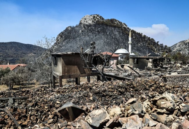 Escombros pós-queimada em uma região do sul da Turquia. Vemos restos de casas, muita pedra e uma montanha ao fundo totalmente desmatada