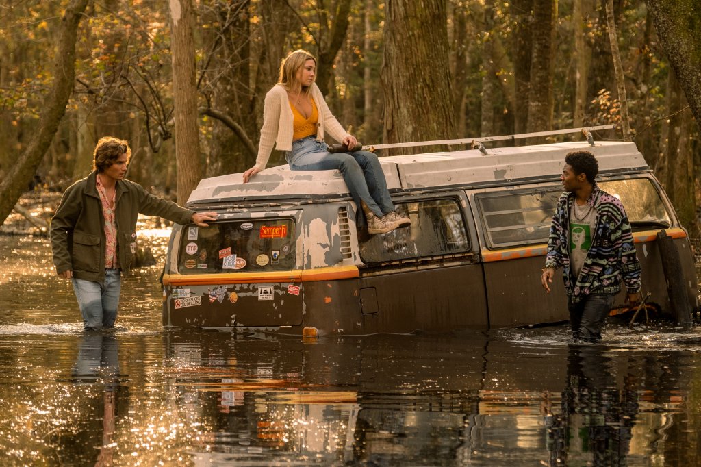 Outer Banks: imagem da segunda temporada com John B., Sarah e Pope; John B. está apoiado na kombi, que está parcialmente submersa e encalhada na água da maré que subiu; Sarah está sentada na parte de cima do veículo enquanto Pope está andando ao lado da kombi com as pernas cobertas pela água