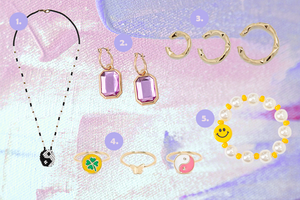 Montagem em fundo lilás e rosa com cinco opções de acessórios. Colar com símbolo yin yang feito à mão, brinco lilás, ear hooks dourados, kit de três anéis e pulseira de pérolas com carinha feliz.