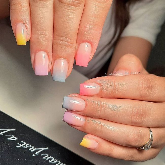 Foto de duas mãos com foco nas unhas decoradas no estilo baby boomer multicoloridas.