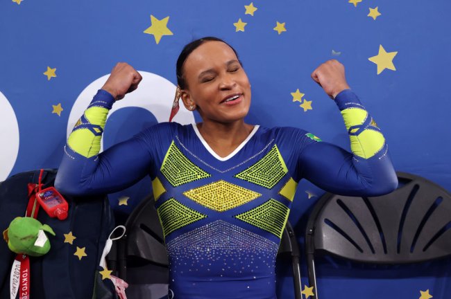 Rebeca Andrade celebrando conquista em Tóquio com os braços em muque. Ela veste um collant azul e amarelo.