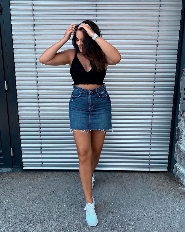 saia jeans com top preto Jovem posando com top preto, com as duas mãos na cabeça, seu cabelo cobre seu rosto e ela olha par ao lado direito.