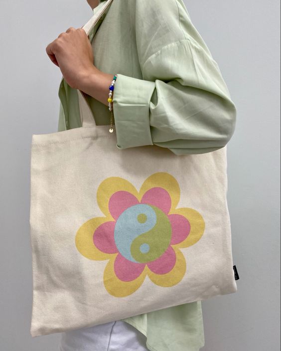 totebag-ecobag Foto do look de uma mulher. Ela usa uma camisa verde menta, pulseira colorida e ecobag com estampa colorida.