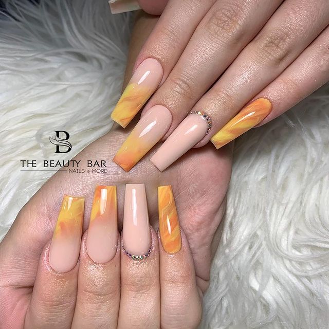 unhas-baby-boomer-laranja Foto de duas mãos com detalhe nas unhas decoradas no estilo baby boomer em um tom de nude e laranja.