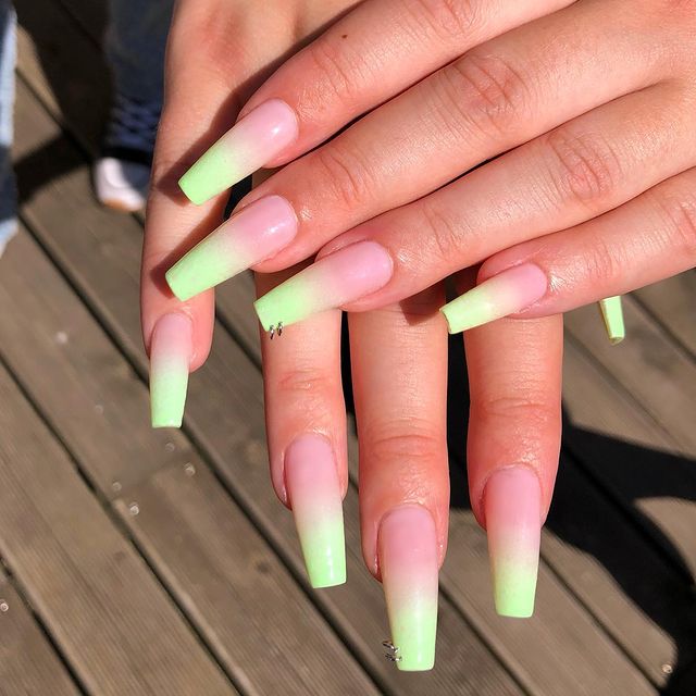 unhas-baby-boomer-verde Foto de duas mãos com foco nas unhas decoradas no estilo baby boomer em um tom de verde claro e detalhe de mini argolas nas unhas dos dedos anelares,