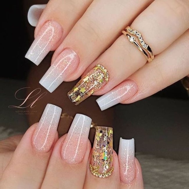 unhas-baby-boomer Foto de unhas pintadas com a técnica baby boomer na cor branca, o dedo anelar está com um anel dourado e decoração dourada na unha.