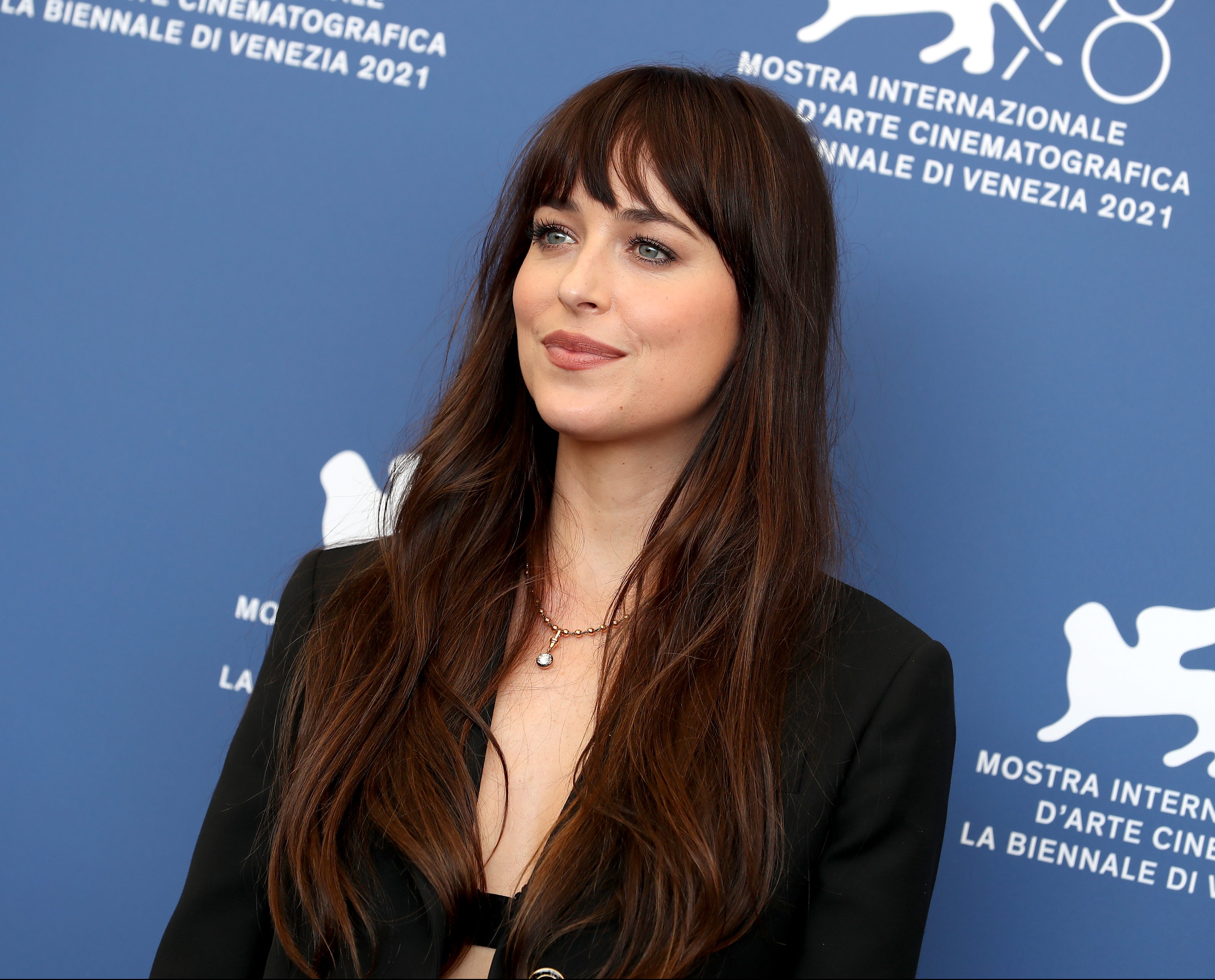 Dakota Johnson posando para foto com fundo azul e com expressão sorridente.