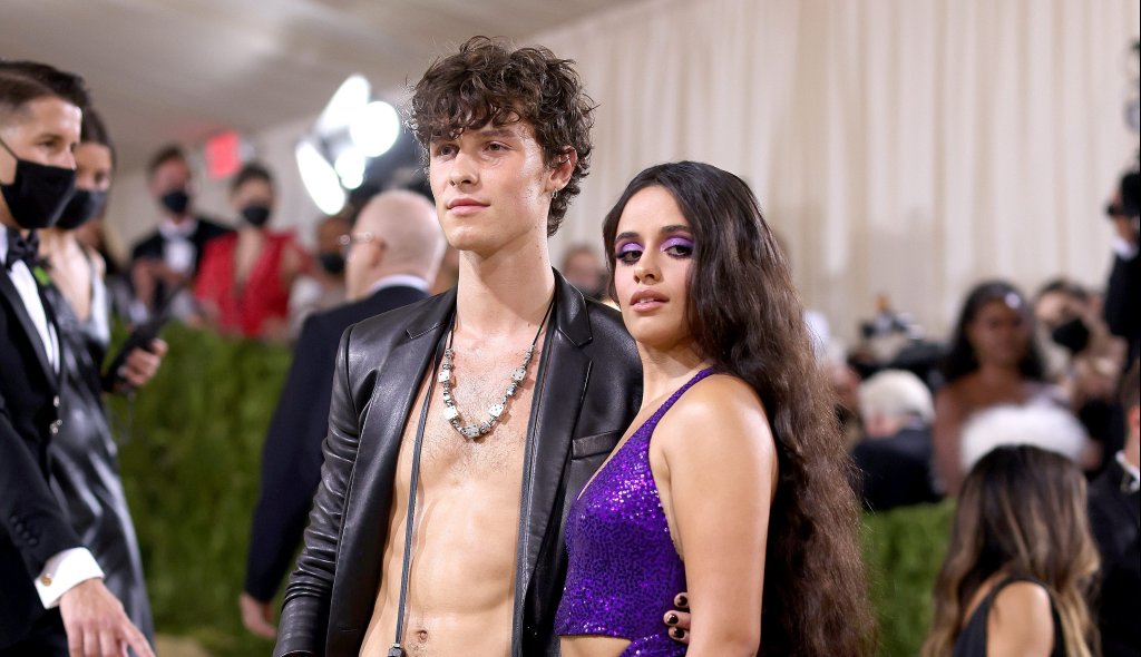 Shawn Mendes e Camila Cabello no MET Gala 2021 posando para foto; ele está sem camisa com uma jaqueta preta e ela usa um look roxo com cabelo solto