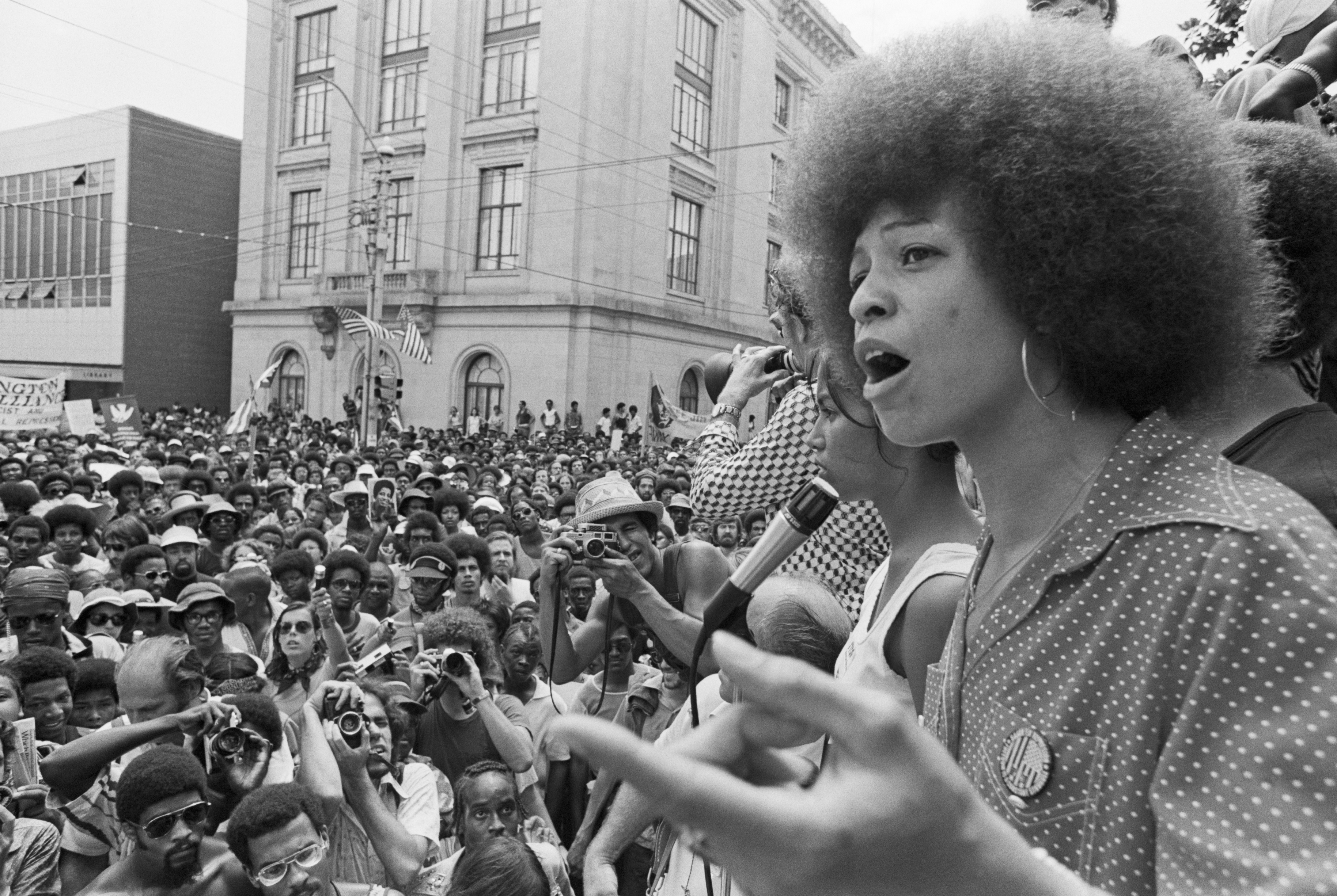 Angela Davis brinco de argola Angela Davis, à direita, discursando para um público em 1974. A foto é em preto e branco.