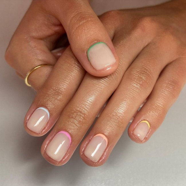 Foto com foco nas mãos, exibindo as unhas com francesinha invertida colorida.