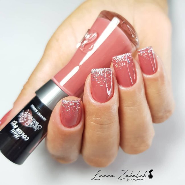 francesinha com glitter Foto de uma mão segurando um esmalte e exibindo as unhas com glitter nas pontas.