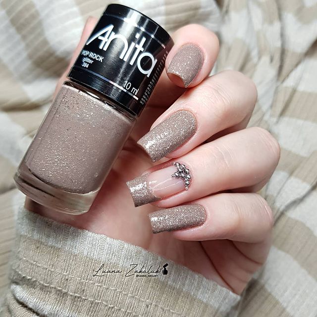 francesinha e unha com glitter Foto de uma mão segurando um esmalte e exibindo as unhas com glitter nas pontas.