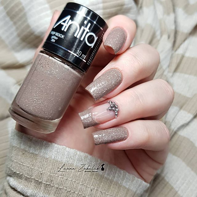 Foto de uma mão segurando um esmalte e exibindo as unhas com glitter nas pontas.