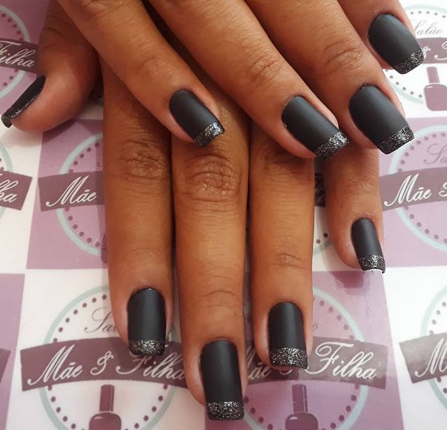 francesinha preta Foto de uma mão segurando um esmalte e exibindo as unhas com glitter nas pontas.