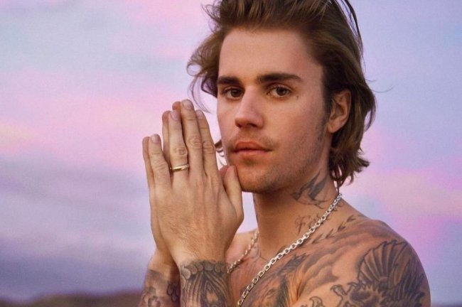 justin-bieber Foto de Justin Bieber para divulgação; ele está sem camisa com as mãos juntas na frente do rosto e olha para câmera com expressão séria