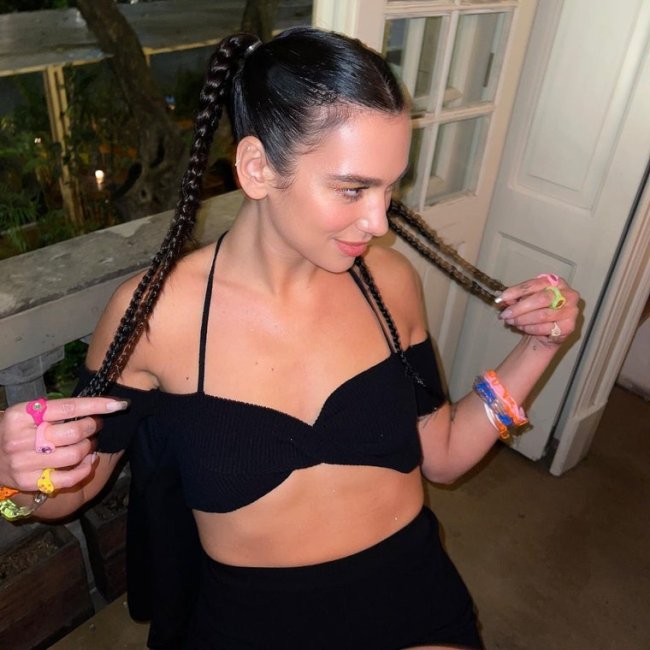 Dua Lipa Cantora Dua Lipa olhando para o lado com top preto e expressão sorridente.
