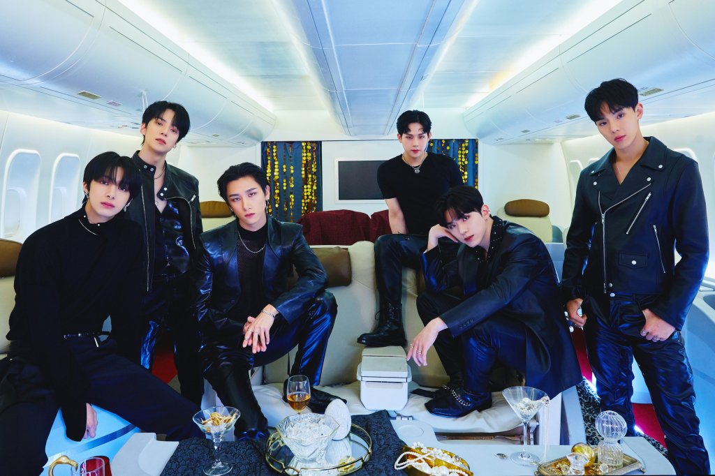 Integrantes do Monsta X posando para foto com fundo azul; eles vestem preto e estão sentados com expressões sérias