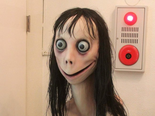 Os 13 bonecos amaldiçoados mais macabros do cinema e da internet Foto da boneca Momo. Ela tem um sorrido maligno de orelha a orelha, olhos esbugalhados e cabelo preto