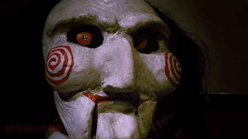 Os 13 bonecos amaldiçoados mais macabros do cinema e da internet Gif do boneco Billy, de Jogos Mortais. Ele é pálido e tem um alvo vermelho desenhado em cada uma das bochechas proeminentes