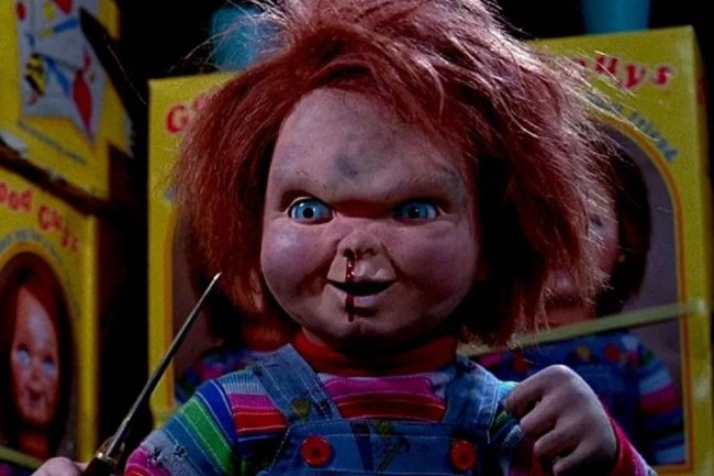 Os 13 bonecos amaldiçoados mais macabros do cinema e da internet Foto do Chucky, o brinquedo assassino. Ele é ruivo, usa um macacão jeans, segura uma adaga e tem sangue escorrendo do nariz