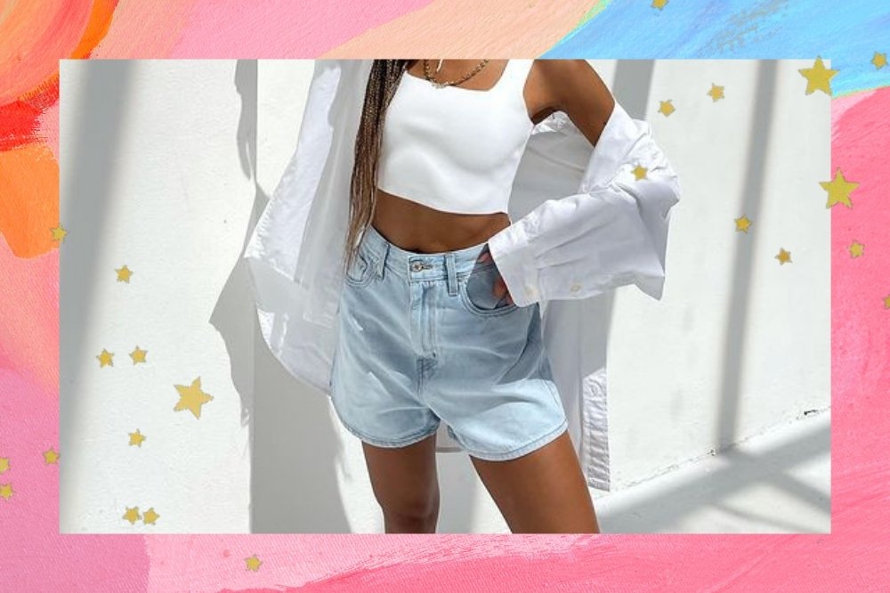 Foto do look de uma mulher com a borda colorida em tons de rosa, azul e laranja com detalhe de estrelinhas douradas. A mulher usa um top cropped branco, camisa branca e short jeans.