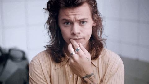harry-styles-gif Gif de Harry Styles. Nele, ele está franzindo as sobrancelhas, com cabelo longo e blusa laranja.