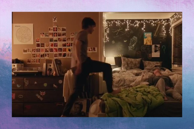 Quarto de Simon, de Com Amor, Simon; ele está subindo na cama com um pé apoiado no colchão e em uma mata verde limão enquanto Abby (Katherine Langford) está deitada; as paredes em volta da cama são de lousa verde escura e na parede ao lado é possível ver um mural de fotos instantâneas e quadros distríbuidos pelo ambiente; a iluminação vem de um abajur em útimo plano e luzes pisca pisca no teto; a margem é uma textura de degradê de rosa, branco, azul. lilás e roxo