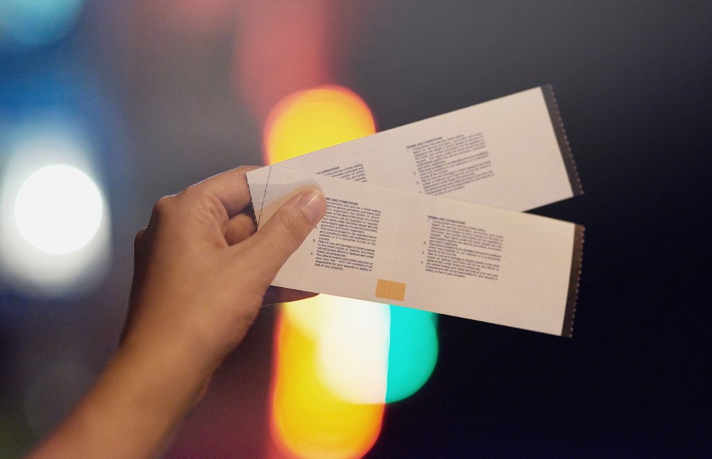 Foto de uma mão segurando dois ingressos para shows