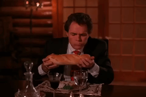 23 provas de que pão é uma das coisas mais maravilhosas que existem Gif de um homem engravatado comendo uma baguete e dizendo que é incrível o sabor
