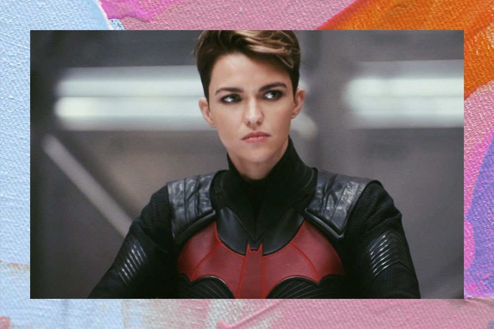 Foto da atriz Ruby Rose na série Batwoman. Nela, ela aparece com o cabelo curto com mechas loiras e traje preto com detalhe de morcego em vermelho.