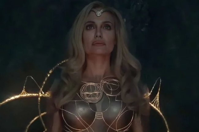 thena Foto de Angelina Jolie como Thena. Nela, ela aparece com cabelos loiros e roupa bege, cercada por linhas douradas mágicas.