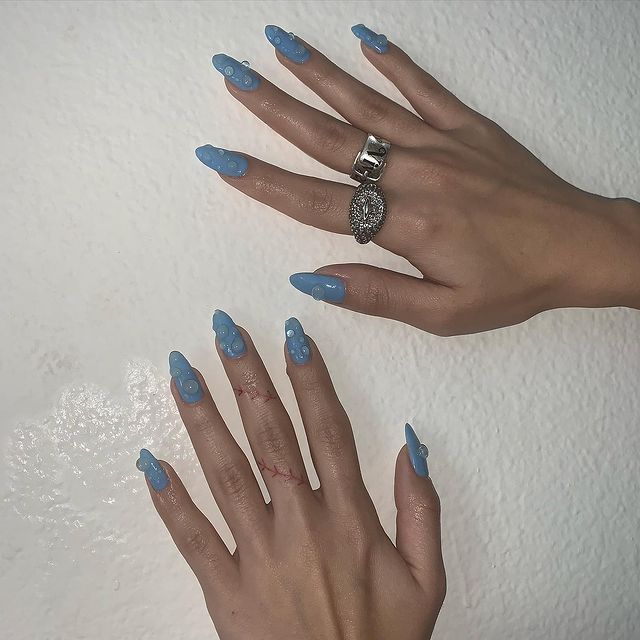 unha-azul-gotas-de-agua Foto de duas mãos com as unhas longas pintadas de azul e detalhe 3D imitando gotas de água.