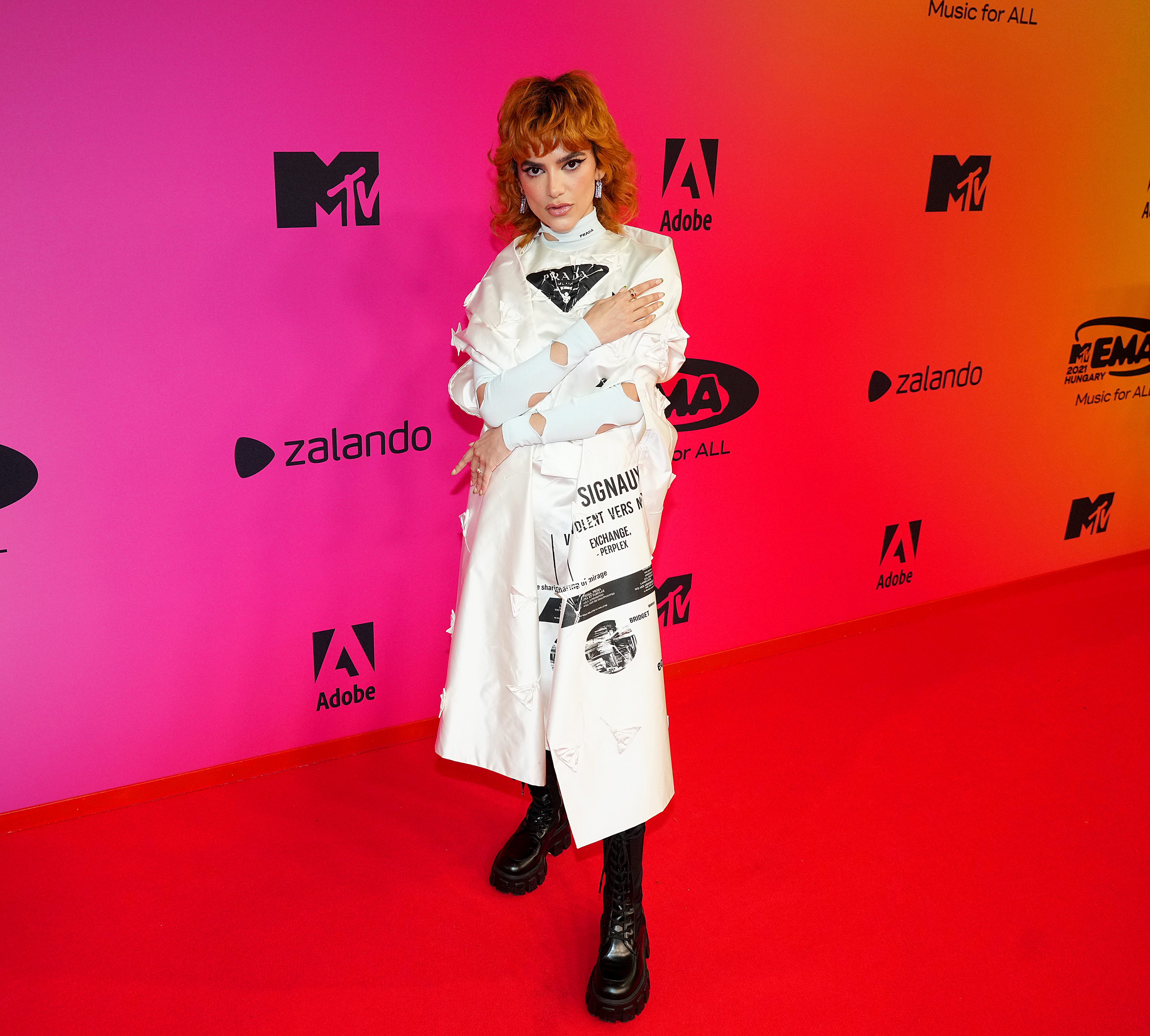 MTV EMAs 2021 – VIP Arrivals Manu Gavassi posando com look branco e bota preta em frente a parede do red carpet durante o MTV EMA na Hungria.