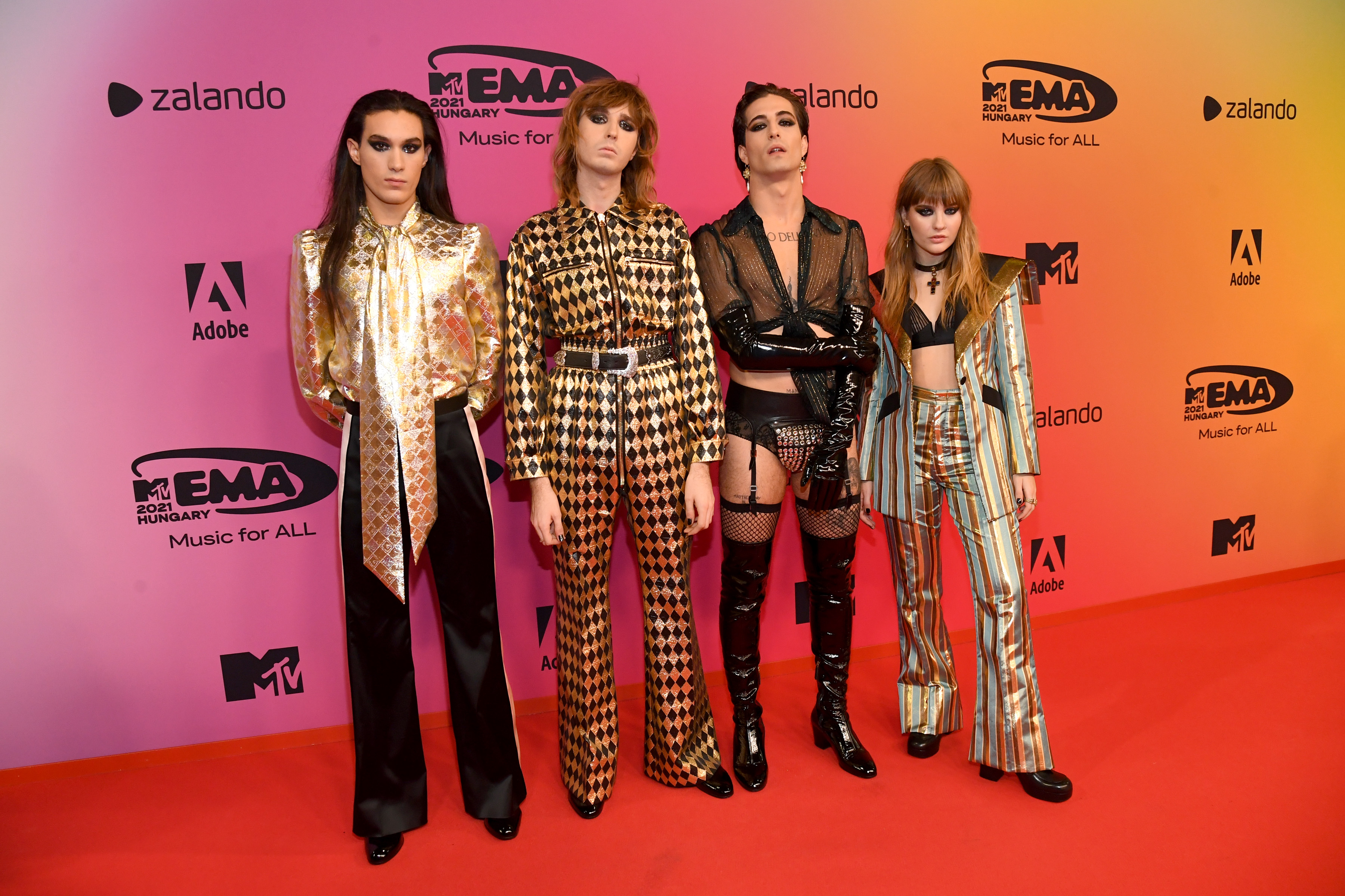 MTV EMAs 2021 – VIP Arrivals Maneskin posando na frente dos logos da MTV EMA com peças diferentes e com transparência.