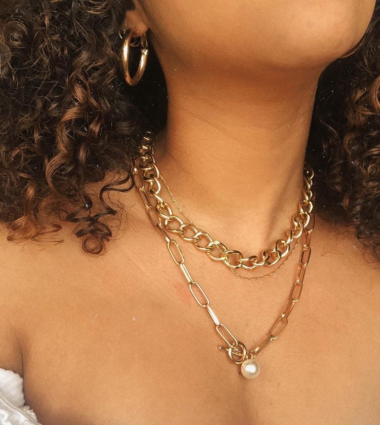 acessorios-dourados-colar-correntes-ladi.elle Garota usando dois colares de correntes. Na foto dá para ver apenas uma parte de seu cabelo cacheado e um brinco de argola na orelha
