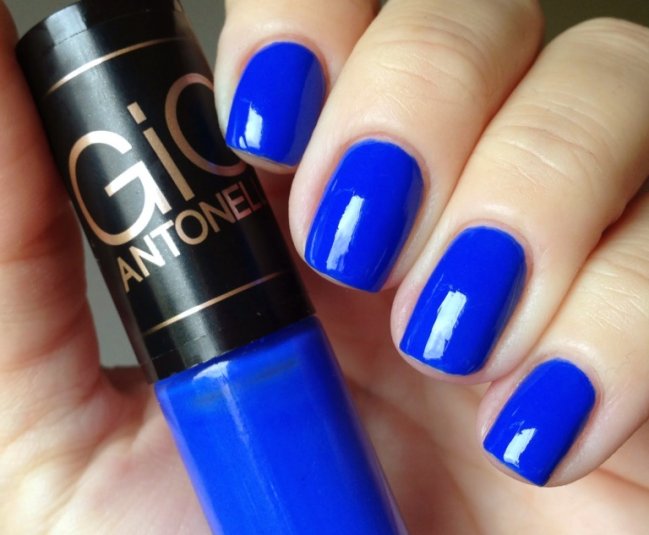 esmalte azul Foto de uma mão segurando um esmalte azul da marca Gio Antonelli com as unhas da mesma cor.
