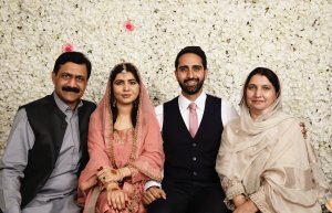 Malala se casa em uma íntima e tradicional cerimônia muçulmana; veja fotos Foto do casamento de Malala. A família está reunida em frente a uma parede de rosas brancas. Todos sorriem.