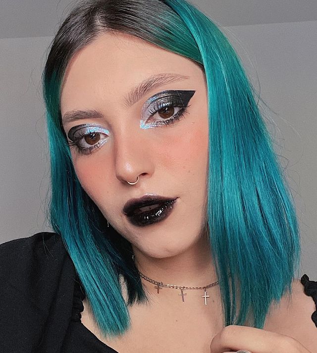 maquiagem-com-batom-preto-e-gloss Selfie de uma mulher. Ela usa o cabelo azul e curto solto e liso, maquiagem com delineado azul e preto com batom preto com gloss. Ela olha para a câmera e não sorri.