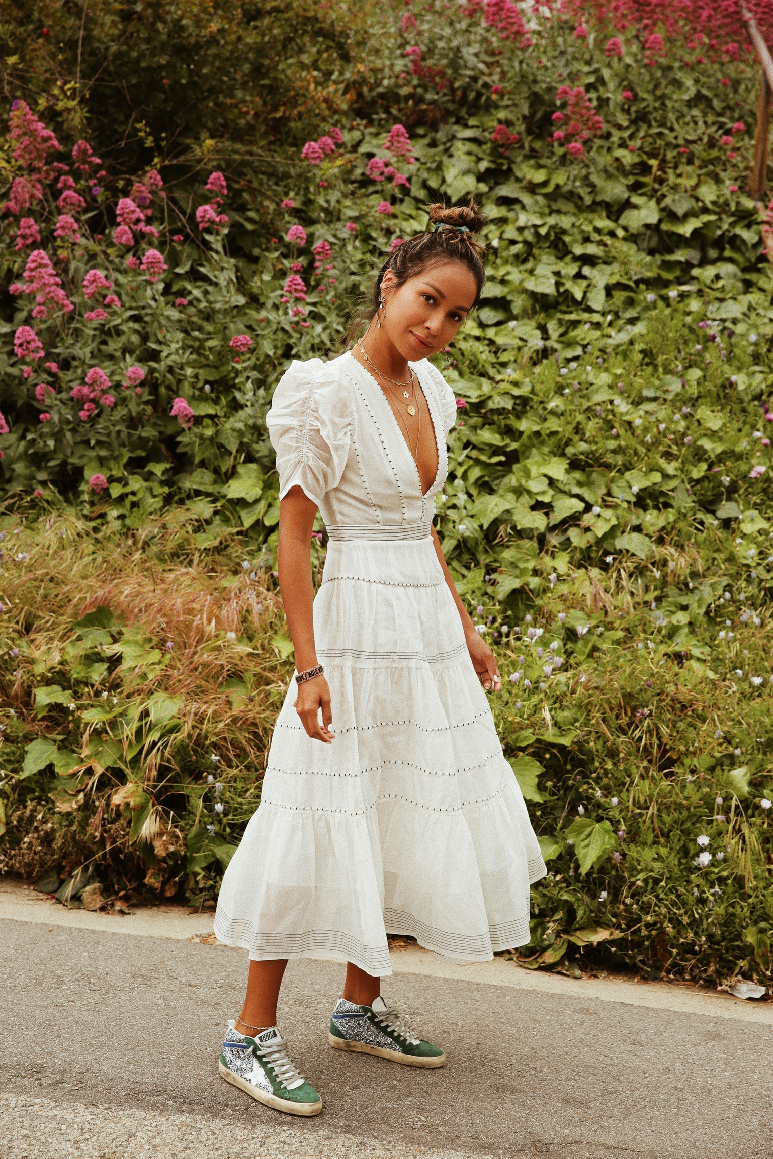 Garota usando vestido branco longo com tênis em fundo com plantas