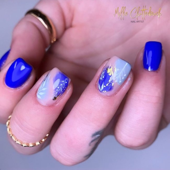 nail-art-cor-pantone-2022 Foto de uma mão com anéis dourados no dedo polegar e médio com as unhas decoradas em tons de azul.