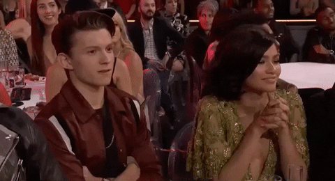 tom-holland-zendaya Tom e Zendaya sentados em uma premiação rindo, enquanto ela faz um gesto com o polegar em forma de 'certo'.