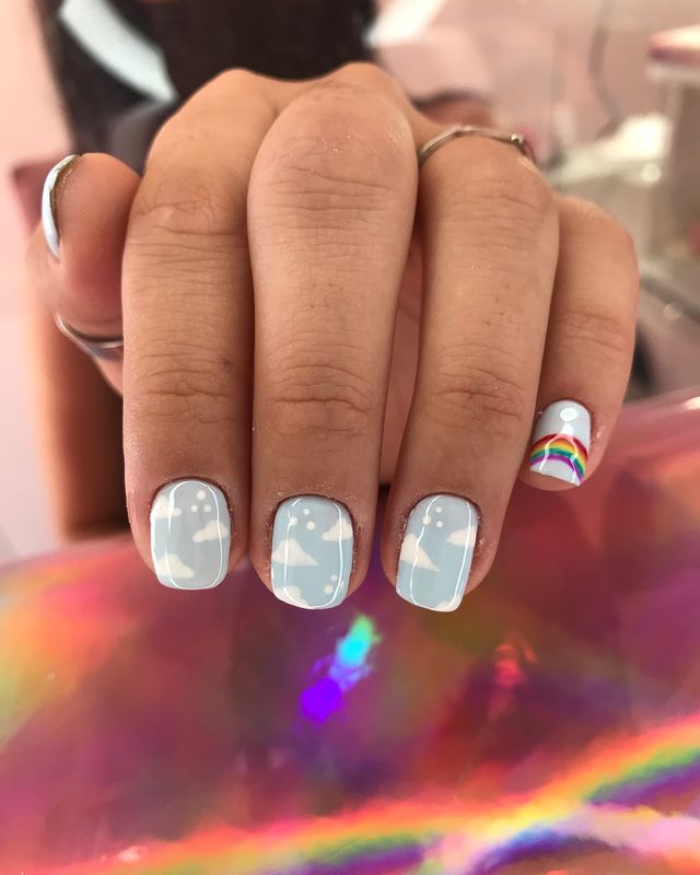 Foto de uma mão com as unhas com esmalte azul e decoração de nuvens brancas.