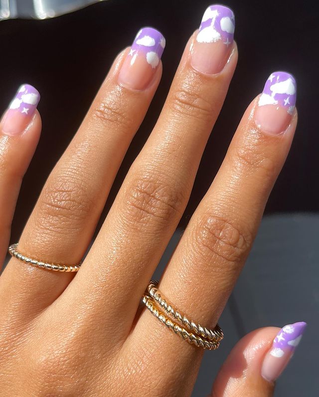 Unhas com esmalte roxo nas pontas e decoração de nuvens brancas.