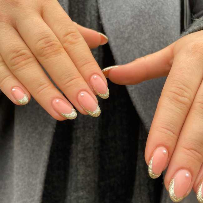 Foto de unhas decoradas com francesinha de glitter dourado e aplicação simples de pérola.