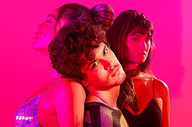 lov3 Três pessoas formando um círculo posando para foto com uma luz rosa ao fundo.